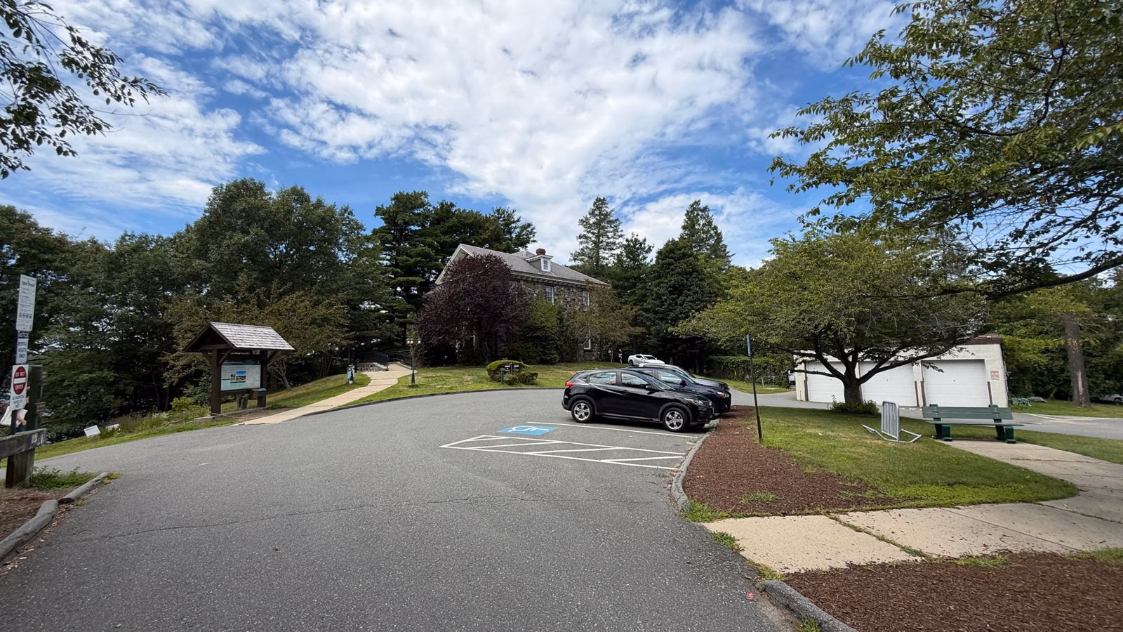 Small parking lot with an accessible space and trail kiosk below the Botume House, Stoneham