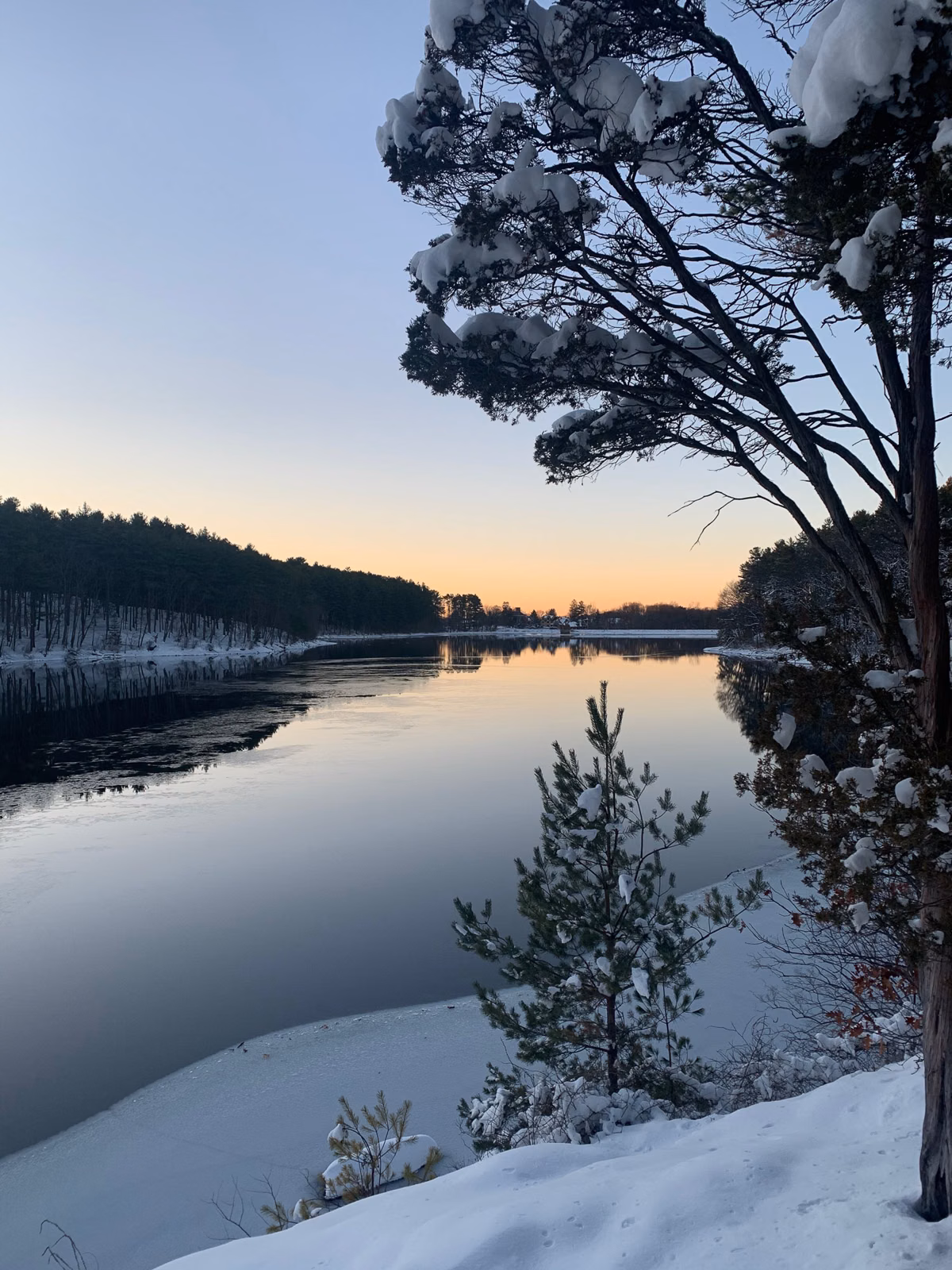 Snow-lined shore and calm water at sunset on the Middlesex Fells reservoir in Stoneham, MA
