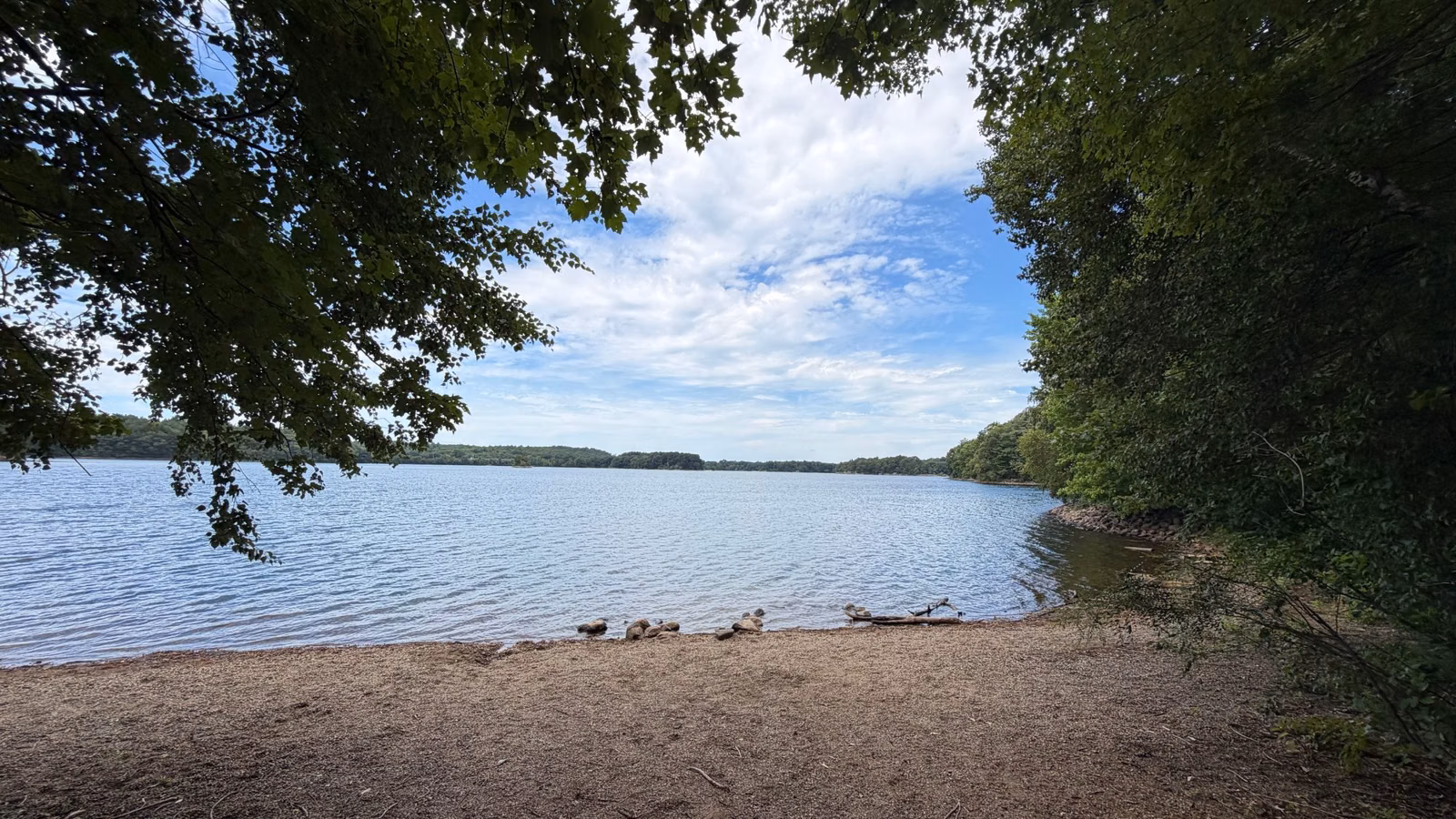 Sandy shore and calm water at Spot Pond under summer clouds, Stoneham