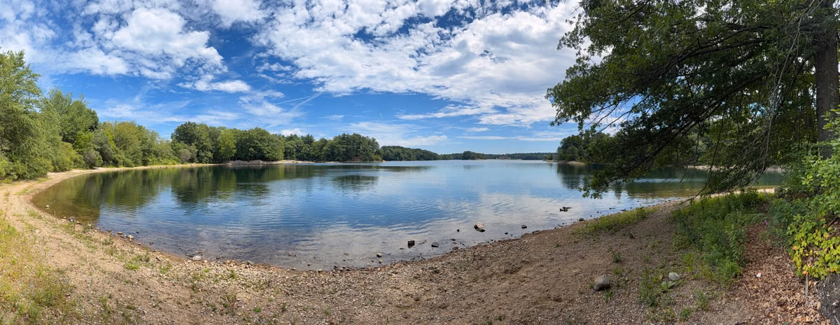 Panorama of Spot Pond curving away under a blue summer sky, Stoneham